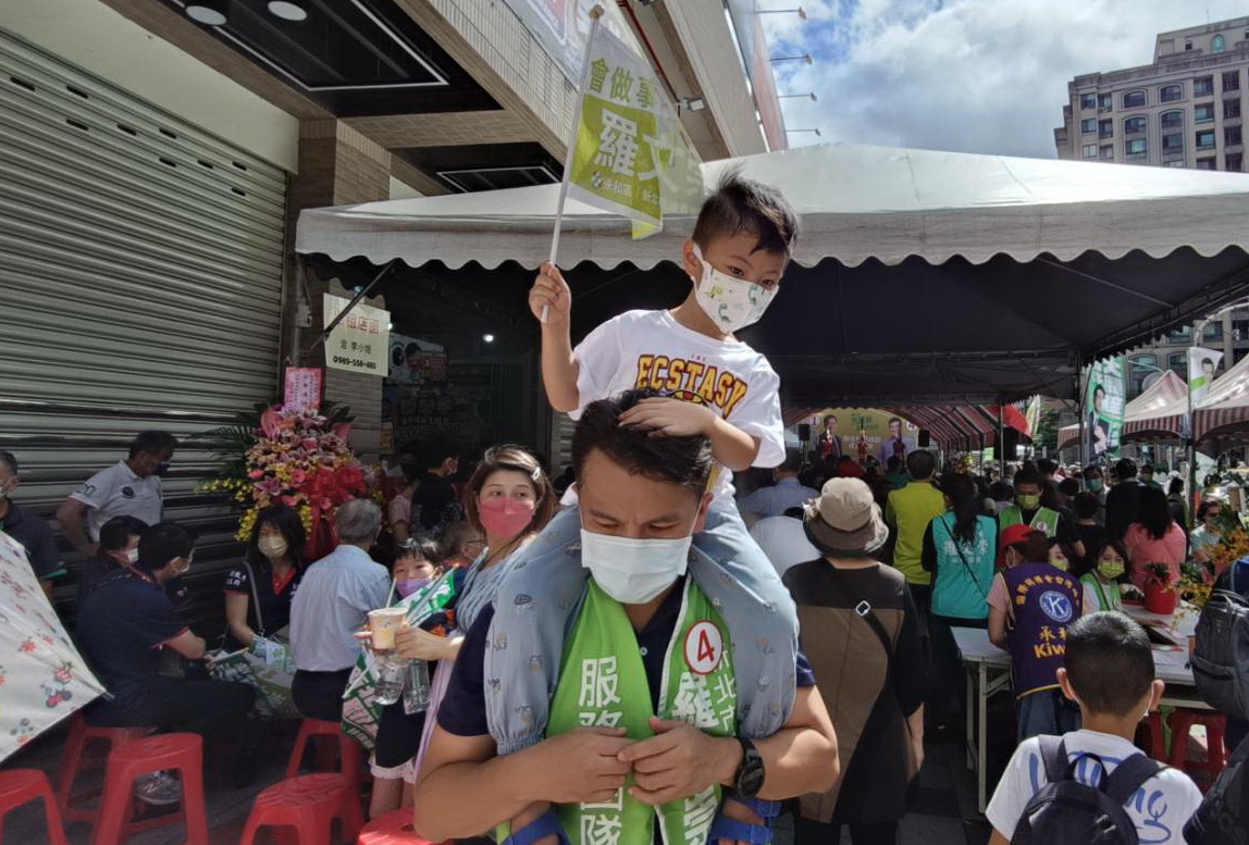 圖片說明:力挺!一名工作人員扛著小孩到場爭取連任的市議員參選人羅文崇造勢。(記者宋紹誠攝)