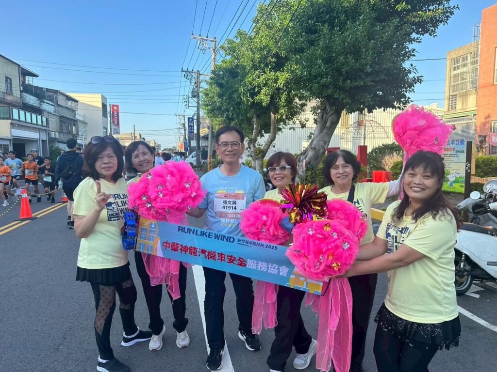 在新竹城市馬拉松賽道旁,理事長張文興與熱情的加油團合影,現場以鮮豔應援道具為跑者加油,營造滿滿活力與歡笑的路跑氛圍。(圖/記者張家燁翻攝)