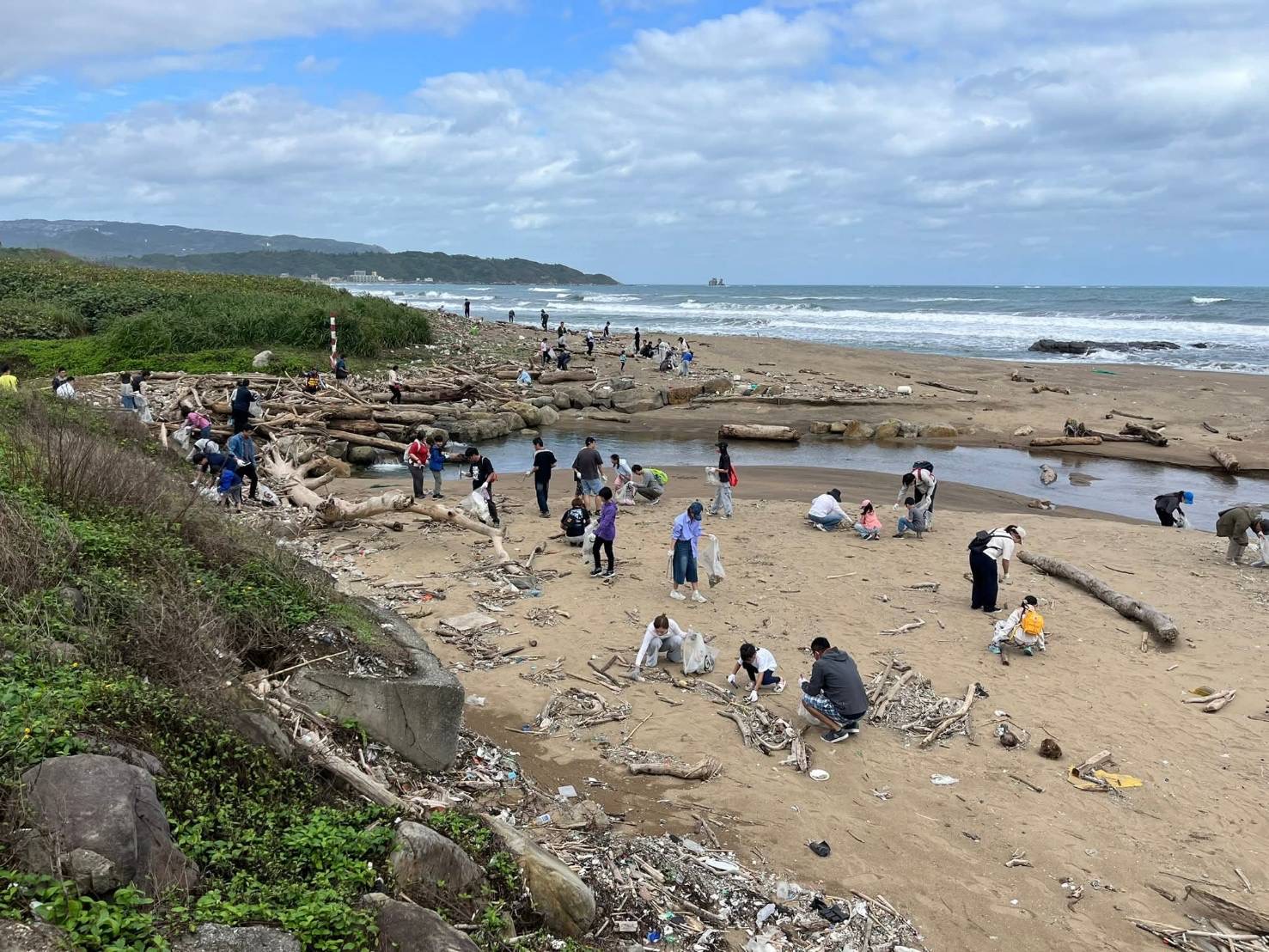 颱風過後的北海岸堆滿漂流物,各企業團隊與家庭成員分布海灘各處投入清理行動。(圖/新創總會提供)