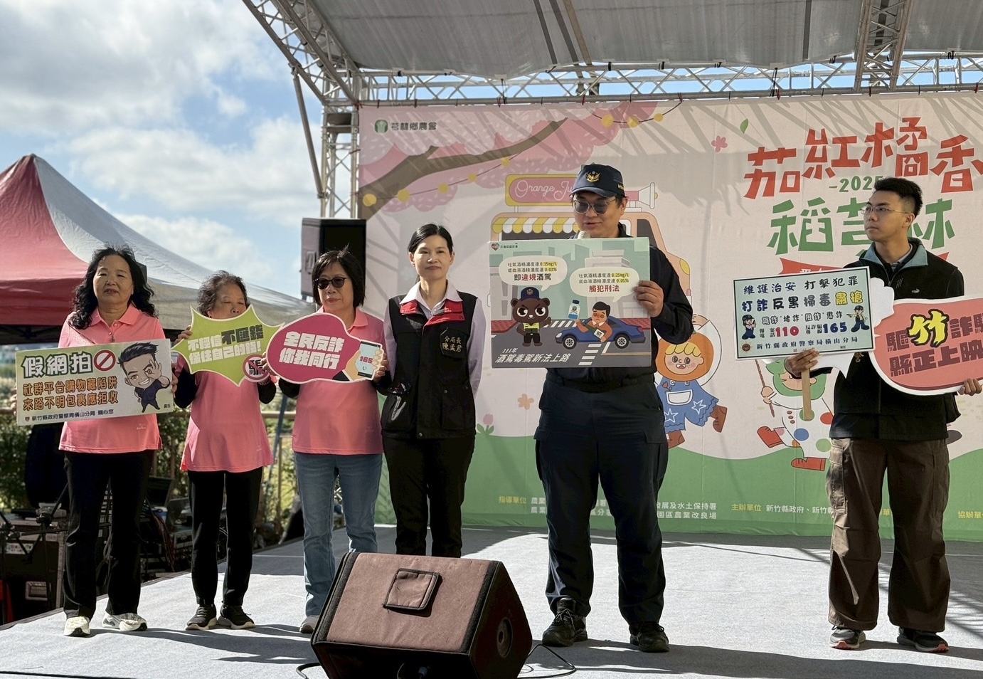 橫山分局結合芎林農會於「茄紅橘香稻芎林番茄產業文化活動」進行反詐與交通安全宣導，分局長陳孟君與同仁手持識詐、反毒駕等宣導標語，透過互動方式提醒民眾提高警覺，共同守護社區安全。（圖/記者張家燁翻攝）