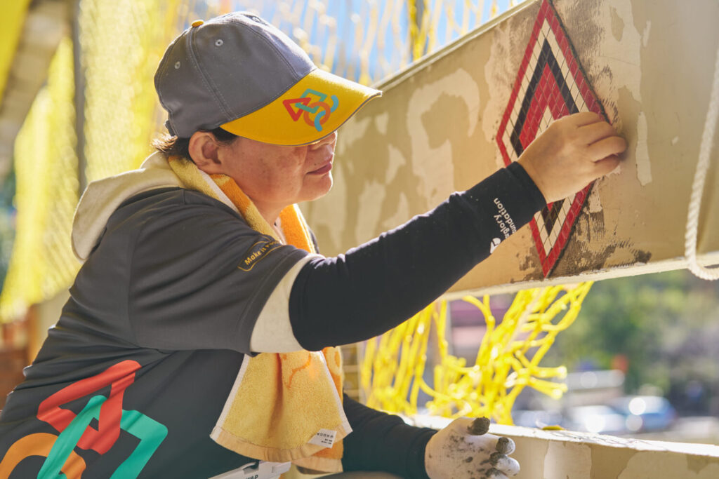 遠雄志工在二樓女兒牆，利用馬賽克磚貼上代表泰雅族文化的「祖靈之眼」。(圖／遠雄文教公益基金會 提供)