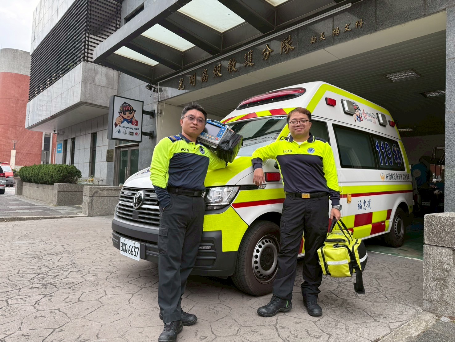 新竹縣政府消防局光明高救隊資深高級救護技術員李均祈(左)、許嘉雄(右)，為此次新竹縣首例院前葉克膜成功搶救的重要關鍵人物，於分隊前與救護車合影，展現第一線救護專業與守護生命的使命感。（圖/記者張家燁翻攝）