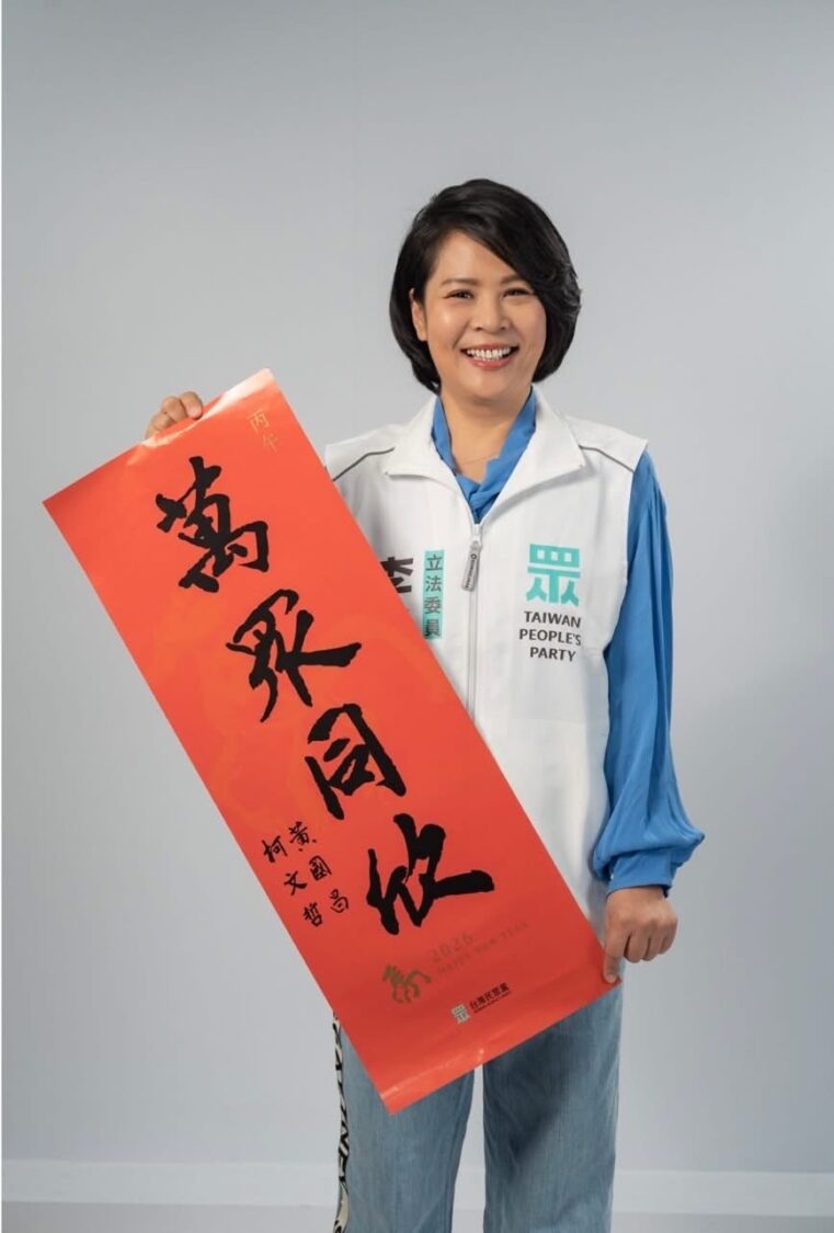 李貞秀身穿台灣民眾黨立委背心，手持春聯拍攝形象照。（圖／翻攝畫面）