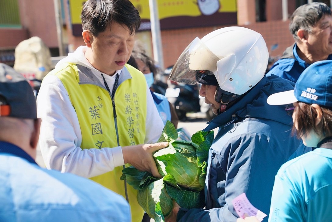 香山區樂齡學習中心主任葉國文於活動現場親自發放高麗菜給民眾，以實際行動支持青農、關懷弱勢。（圖／記者林照東翻攝）