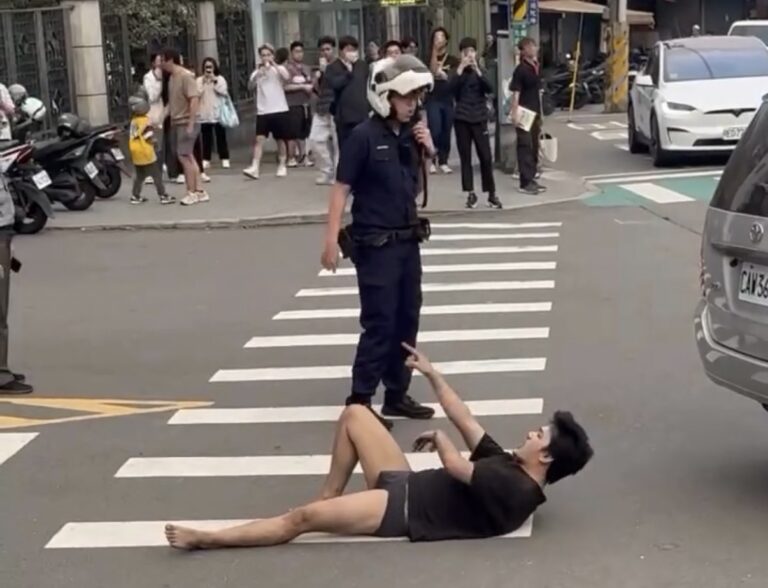 警方於現場掌控情勢，一名男子倒臥在斑馬線上情緒激動，現場聚集不少民眾圍觀，畫面一度緊張。（圖／翻攝畫面）