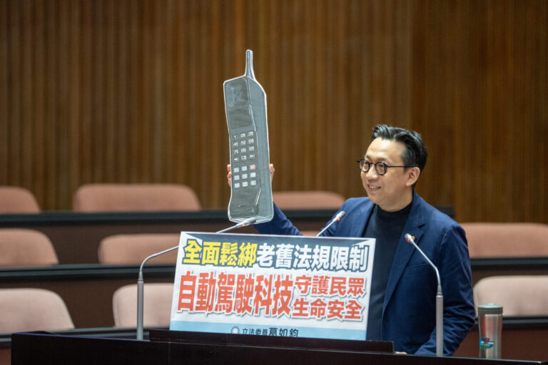 立法委員葛如鈞今日於立法院總質詢行政院長卓榮泰時拿出1980年代「黑金剛」手機(道具),諷刺台灣車輛科技法規落後。(圖/葛如鈞國會辦公室)