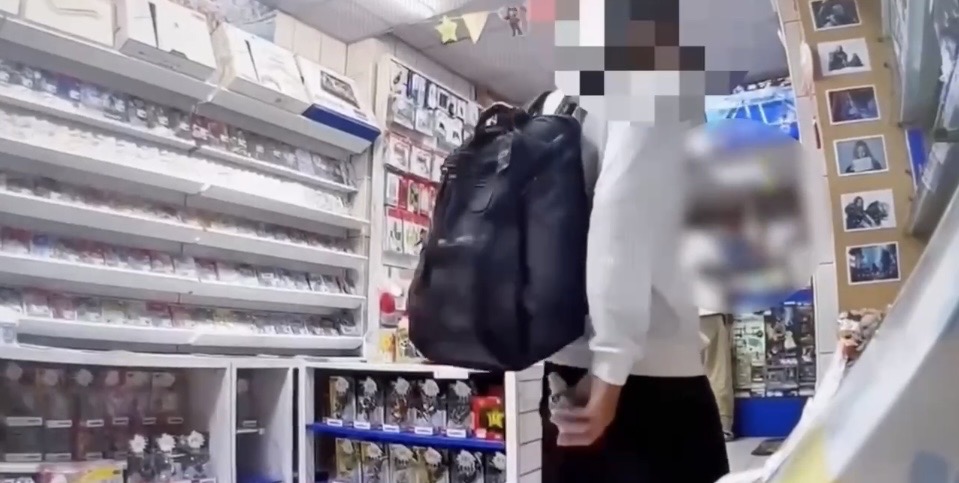 男子將店內展示櫃內之PS5手把放入後背包與衣服之間的影像截圖。（圖／記者 趙靜姸翻攝）