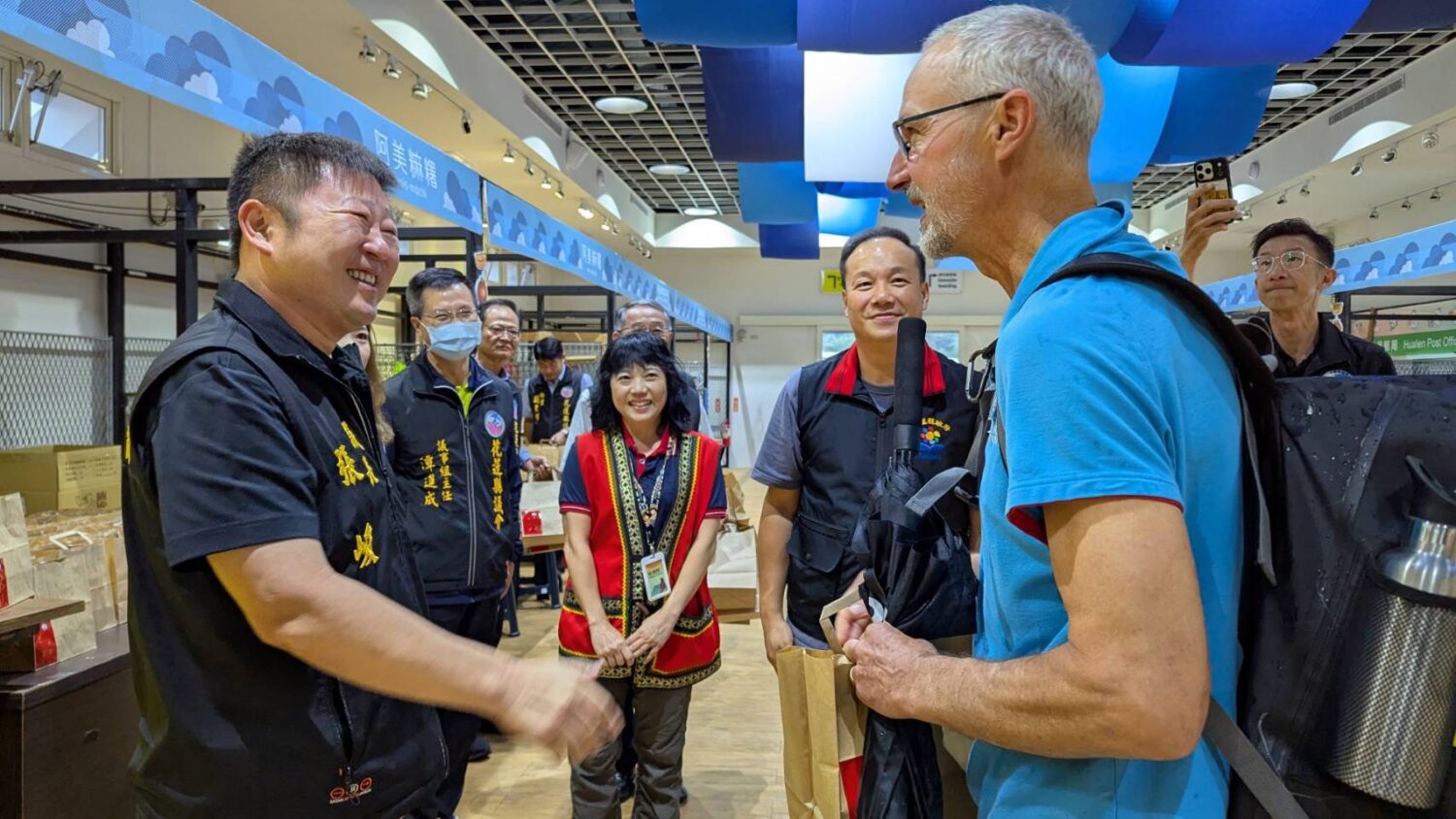 張峻（左一）贈送每位旅客一包由萬榮鄉支亞干部落青年親手栽種有機山蘇製成的山蘇茶包，希望讓更多國際友人認識花蓮原住民族文化與在地品牌。（圖／記者 趙靜姸翻攝）
