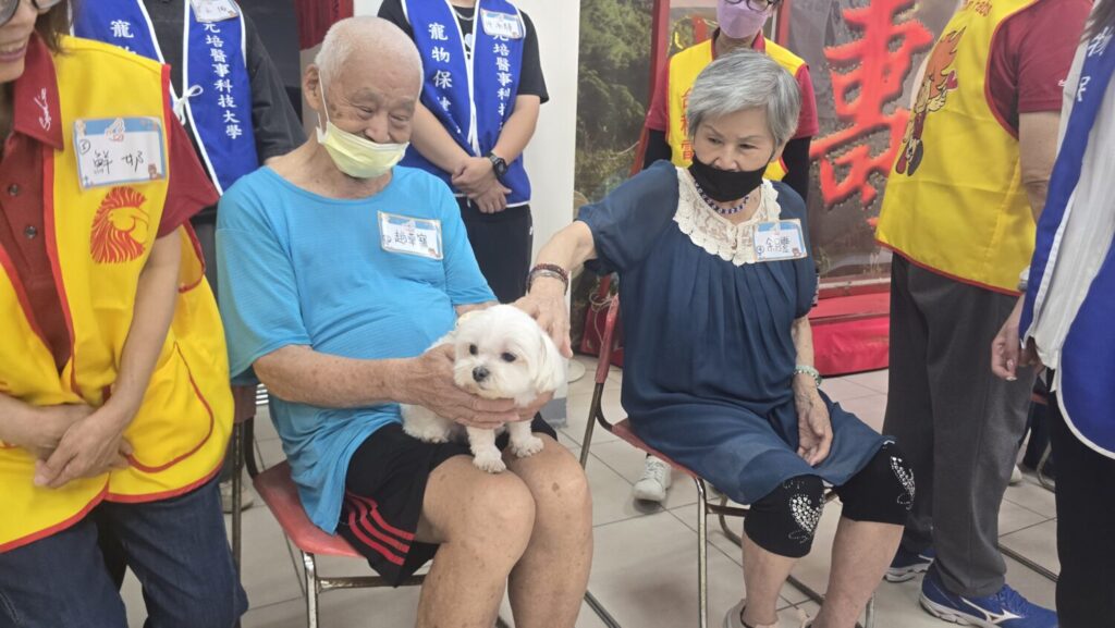長輩在志工與學生的陪伴下,親手餵食心輔犬,透過手部動作訓練精細肌肉控制,也從照顧毛小孩的過程中獲得成就感與自信心。(圖/台積電慈善基金會提供)
