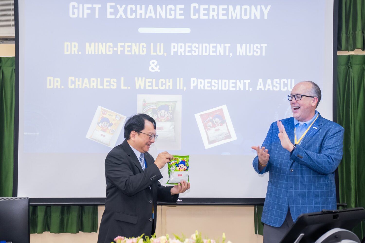 明新科大校長呂明峯(左)致贈綠色包裝「乖乖」予AASCU主席 Dr. Charles L. Welch II(右),並分享臺灣科技圈祈求機台「乖乖運轉」的趣味文化。(圖/明新科大提供)