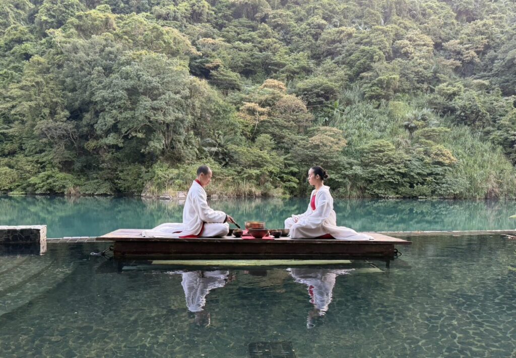 把喧囂留給遠方,把寧靜留給此刻。「棋不語」表演者對坐水上木筏,以聲響展開對話,倒影與天光共同入戲。(圖/馥蘭朵烏來提供)